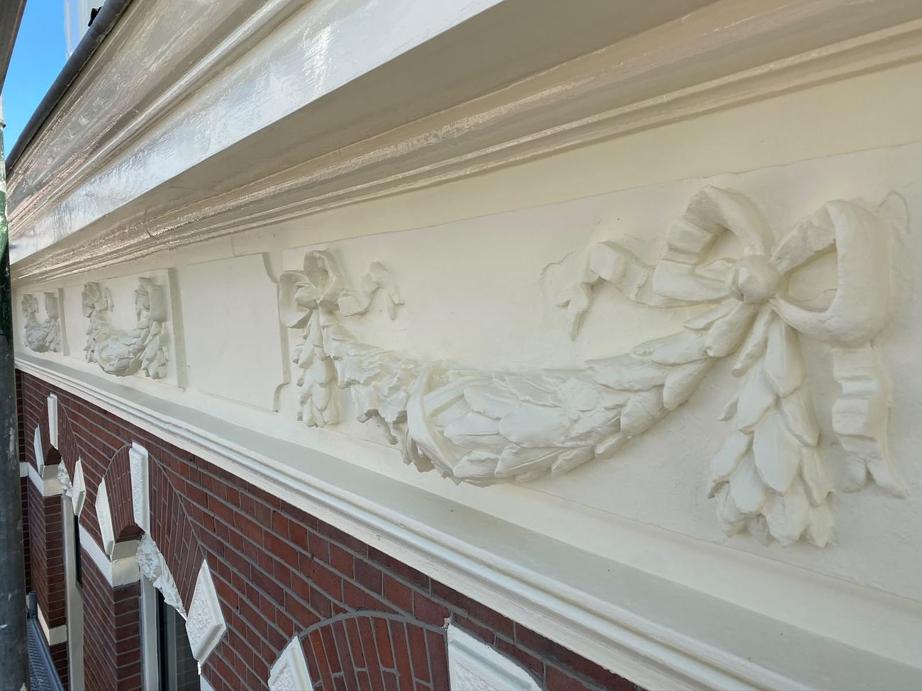Gerestaureerd sierpleisterwerk in de gevel, wit geschilderd